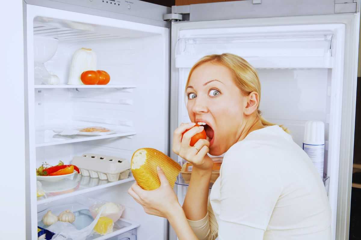 Donna che mangia davanti al frigo