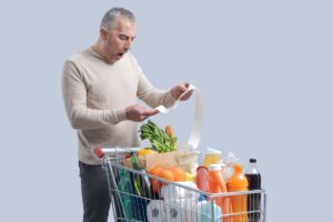 Uomo con carrello che guarda con aria stupita lo scontrino della spesa