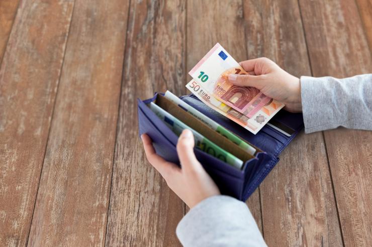 uomo con portafogli aperto sul tavolo conta le banconote