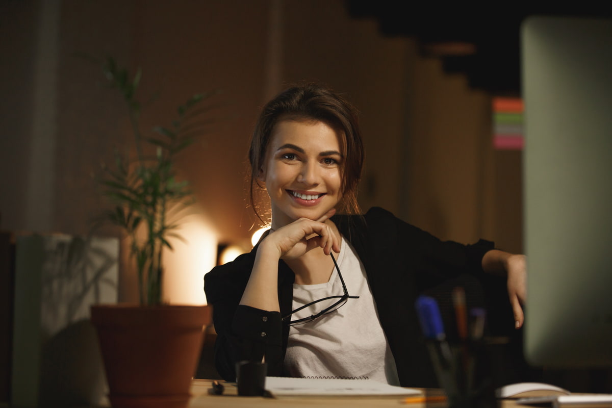 Donna che sorride seduta alla scrivania di sera